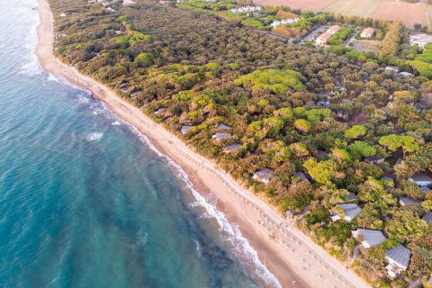 Aerial photo of mobile homes nestled in lush trees near a sunny sandy beach with clear blue ocean waters.