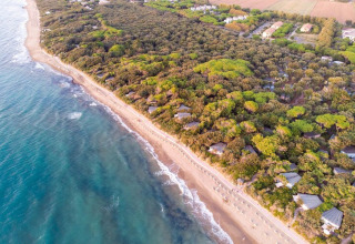 Vista aérea de casas móviles entre árboles cerca de una playa de arena y aguas claras del mar en un entorno natural.