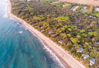 Aerial photo of mobile homes nestled in lush trees near a sunny sandy beach with clear blue ocean waters.