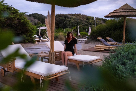 Mujer sentada en una tumbona bajo sombrilla en el Holiday Resort Riva degli Etruschi, Italia, cerca del mar.