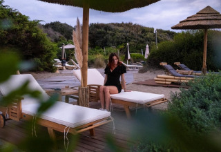 Woman sitting on a sunbed under umbrella at Holiday Resort Riva degli Etruschi in Italy, close to the sea.