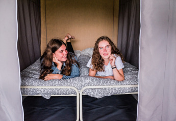 Deux jeunes femmes allongées sur un lit dans une tente safari, souriantes et profitant de l’ambiance cosy.