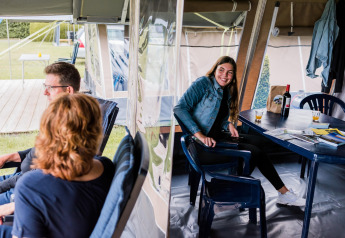 Trois personnes se détendent dans une tente safari, une femme sourit à table entourée d’affaires de camping.