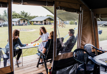 Familie spiller brætspil i safari-telt på Camping Nommerlayen 1 i Luxembourg med grøn udsigt udenfor.