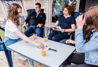 Famille détendue dans une tente safari, deux jeunes jouent à un jeu de société avec quatre verres de jus.