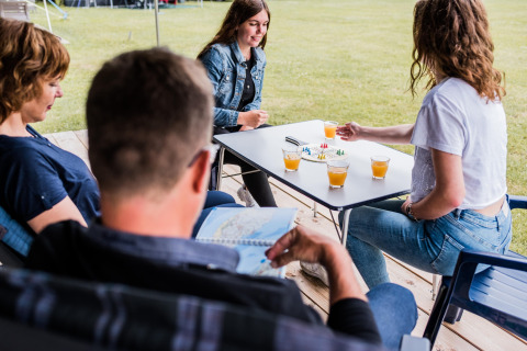 Vier mensen ontspannen in een safaritent, drinken sap en spelen een bordspel aan een tafel.