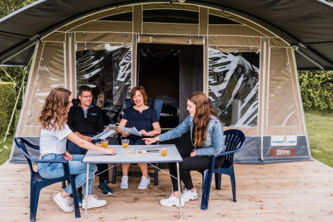 Famiglia gioca a un gioco da tavolo con bevande davanti alla tenda safari Camping Nommerlayen 1 in Lussemburgo.