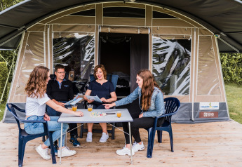 Familie nyder et brætspil foran safari-teltet Camping Nommerlayen 1 i Luxembourg med juice og glæde.