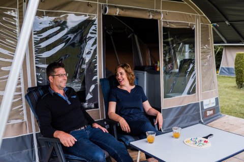 Un couple se détend devant une tente safari, partageant un jus et un jeu de société sur une table.