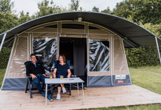 Due persone si rilassano davanti a una tenda safari al Camping Nommerlayen 1 in Lussemburgo, circondati dalla natura.