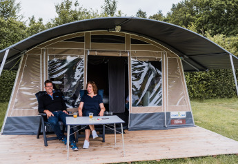 To personer slapper af foran et safari telt ved Camping Nommerlayen 1 i Luxembourg, omgivet af natur.