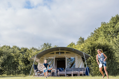 En familie hygger sig med badminton foran et safaritelt på Camping Nommerlayen 2 i Luxembourg.