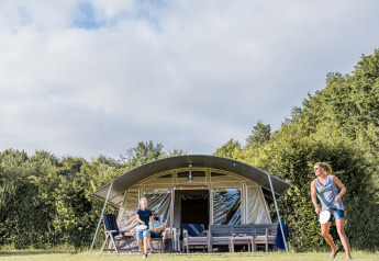 A family enjoys playing badminton in front of a safari tent at Camping Nommerlayen 2 in Luxembourg.