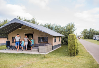 Gezin verlaat een safaritent bij Resort Nommerlayen 3 op een zonnige dag met groen gras en struiken.