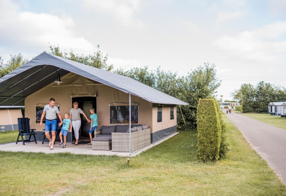 Gezin stapt uit een safaritent bij Resort Nommerlayen 3, zonnige dag, met frisgroene gazon en hagen.