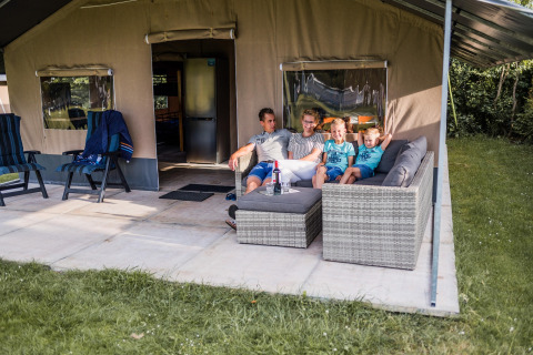 Famille assise sur un canapé devant une tente safari au Resort Nommerlayen 3 au Luxembourg.