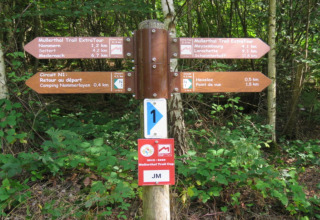Wegwijzer aan Resort «Nommerlayen 3» in Luxemburg, met richtingen voor de Mullerthal Trail en trekpleisters.