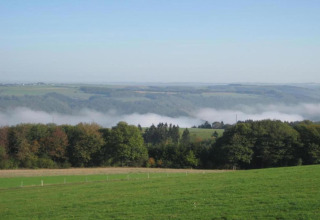 Uitzicht vanuit een safaritent op Resort Auf Kengert 1 in Luxemburg met groene weiden en lichte mist.