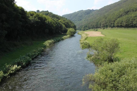 Rivier slingert door groene vallei vlakbij Resort «Auf Kengert 1» in Luxemburg, met weiden en bos.