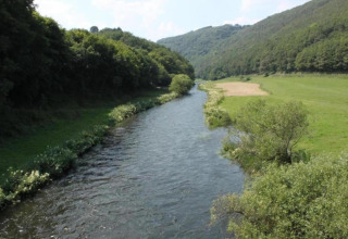 Rivier slingert door groene vallei vlakbij Resort «Auf Kengert 1» in Luxemburg, met weiden en bos.
