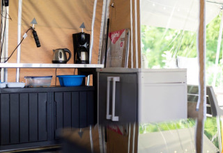 Kleine keukenhoek in een safaritent met koffiezetapparaat, waterkoker, opbergkasten en keukenspullen.