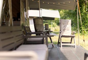 Espace détente extérieur devant une tente safari avec fauteuils confortables sous des auvents ombragés.