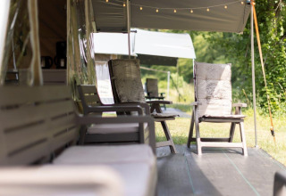 Gezellige buitenzitplek bij een safaritent met comfortabele stoelen en tafeltjes onder een luifel.