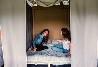 Deux femmes discutent et sourient sur un lit dans une tente safari au Camping Gritt 1 au Luxembourg.