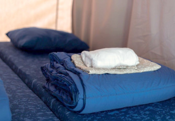 Lit préparé dans une tente safari avec draps pliés, couverture et oreiller, prêt pour les invités.