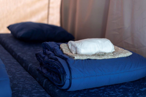 Opgemaakt bed in een safaritent met opgevouwen lakens, deken en kussen, klaar voor gasten.