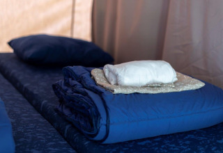 Opgemaakt bed in een safaritent met opgevouwen lakens, deken en kussen, klaar voor gasten.