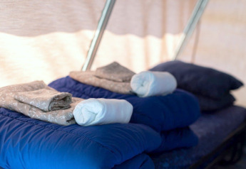 Lits avec sacs de couchage bleus, draps pliés et serviettes dans l'intérieur douillet d'une tente safari.