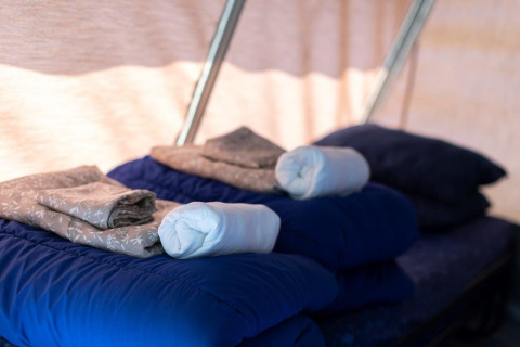 Bedden met blauwe slaapzakken, opgevouwen lakens en handdoeken in het interieur van een safaritent.