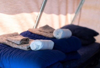 Bedden met blauwe slaapzakken, opgevouwen lakens en handdoeken in het interieur van een safaritent.