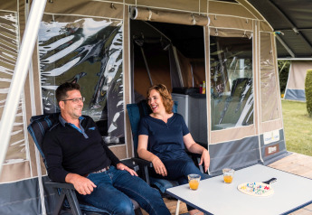 Deux personnes se détendent devant une tente safari au Camping Gritt 1 au Luxembourg, avec jus et jeu de société.