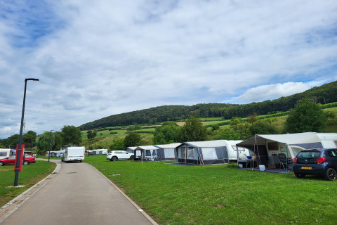 Foto van een camping met safaritenten, auto's en groene heuvels onder een bewolkte lucht.