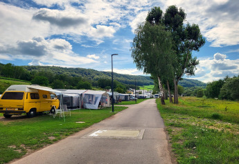Un camping moderne avec des tentes safari et un van jaune, entouré de collines et d'arbres verdoyants.