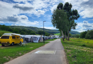 Een moderne camping met safaritenten en een gele camper, omgeven door groene heuvels en hoge bomen.
