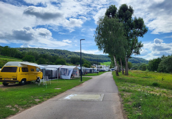 Un moderno campeggio con tende safari e un camper giallo, immerso tra colline verdi e alberi alti.
