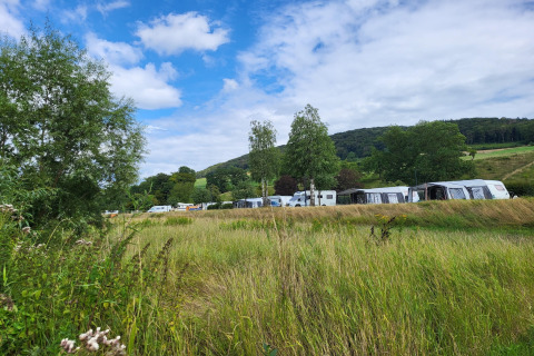 Uitzicht op een safaritent-camping met caravans, omgeven door groene velden, bomen en heuvelachtig landschap.