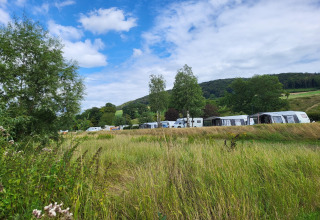 Uitzicht op een safaritent-camping met caravans, omgeven door groene velden, bomen en heuvelachtig landschap.
