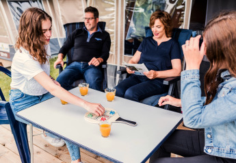 Famille dans une tente safari au Camping Gritt 1 au Luxembourg, jouant à un jeu de société et buvant du jus.