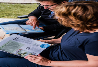 Due persone sedute in una tenda safari al Camping Gritt 1 in Lussemburgo guardano una mappa e una brochure.
