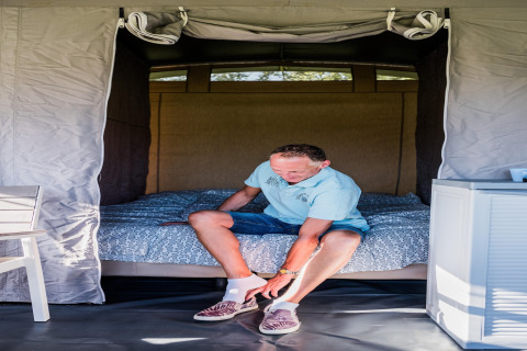 Man doet schoenen aan in een comfortabele safaritent bij Camping Gritt 2 in Luxemburg, zittend op het bed.