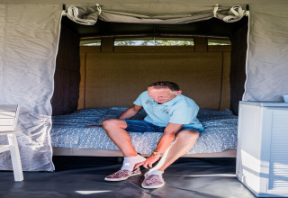 Man doet schoenen aan in een comfortabele safaritent bij Camping Gritt 2 in Luxemburg, zittend op het bed.