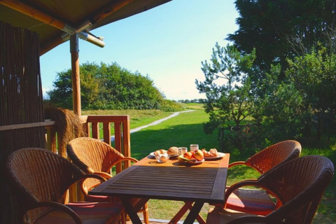 Essbereich im Freien beim Luxus-Safari-Zelt auf Ameland mit Blick auf Wiesen und gedecktem Tisch.