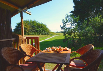 Comedor al aire libre en tienda safari de lujo en Ameland, Países Bajos, con desayuno y vista natural.