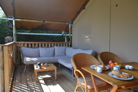 Porche cubierto con sofá, mesa de comedor y desayuno en una lujosa tienda safari en Ameland.