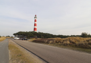 Luksussafari-telt på Ameland, Holland. Fyrtårn med røde og hvide striber, omgivet af klitter og vej.