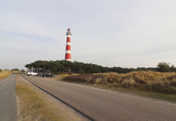 Luksussafari-telt på Ameland, Holland. Fyrtårn med røde og hvide striber, omgivet af klitter og vej.